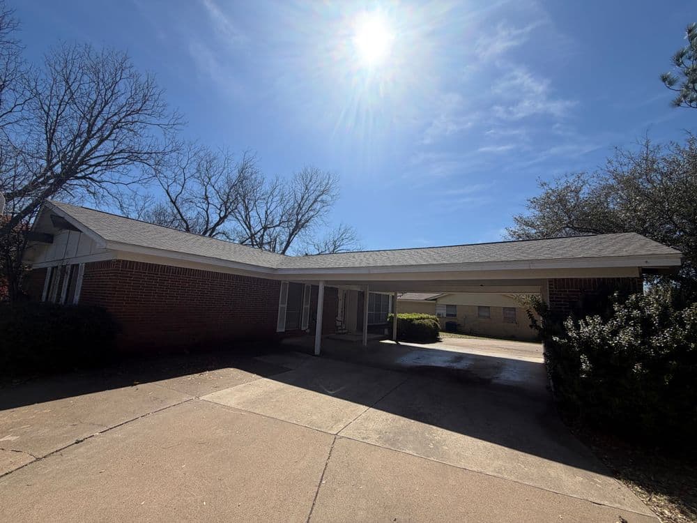 Single-story brick house with a wide driveway under a clear blue sky.