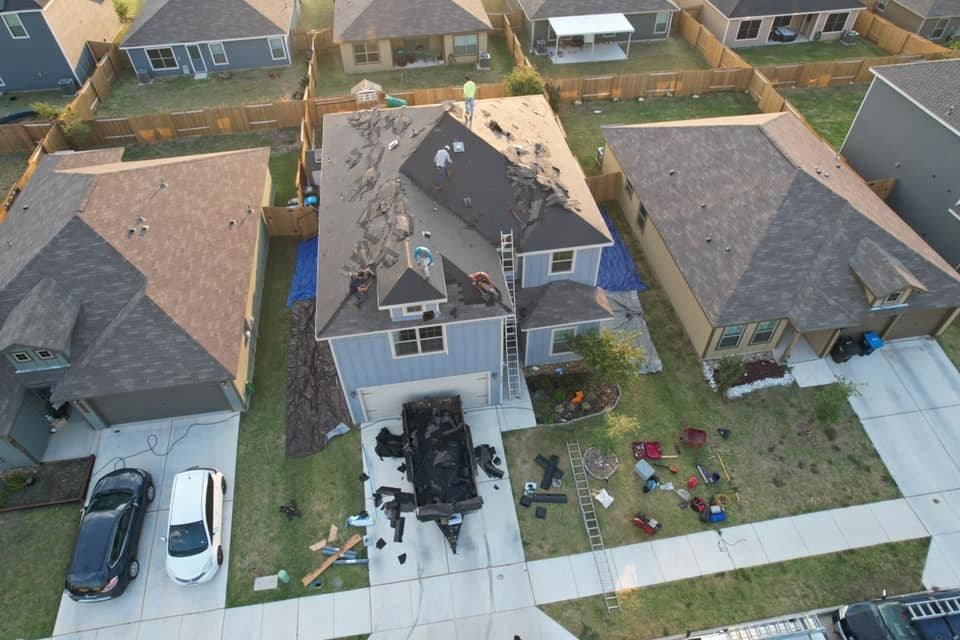 Aerial view of a house under roof repair with workers, tools, and vehicles in the driveway.