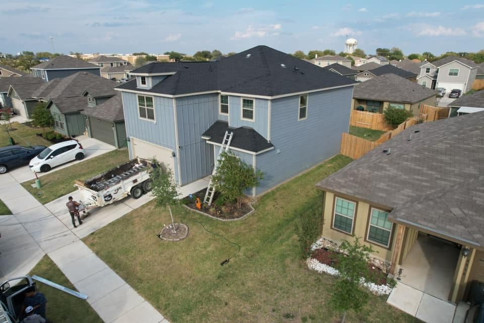 Aerial view of a blue two-story house with a ladder, surrounded by other homes and grass.