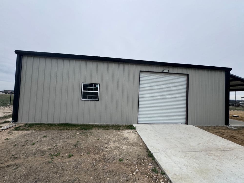 Metal storage building with a roll-up door and a window, set on a gravel surface.