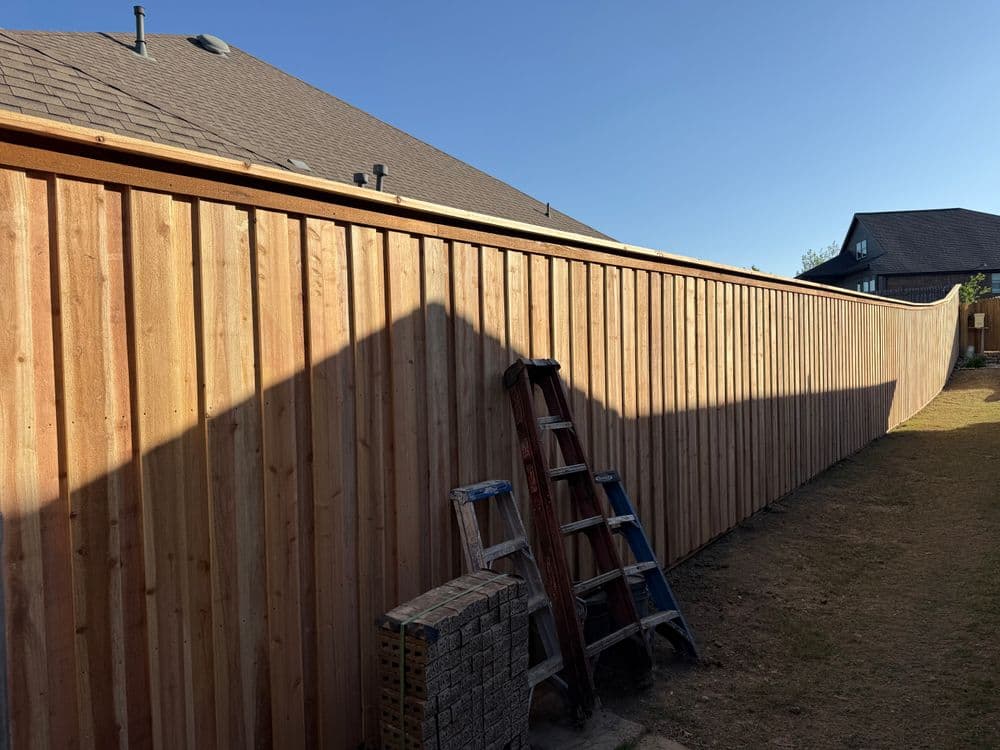 New wooden privacy fence installed in a backyard, with a ladder and stone blocks nearby.
