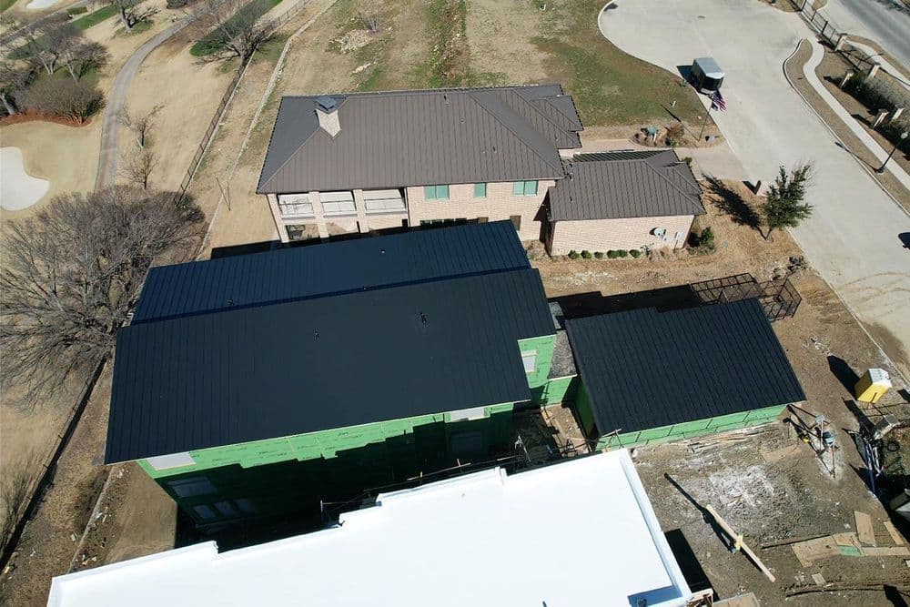 Aerial view of residential homes with black roofs and green siding under construction.