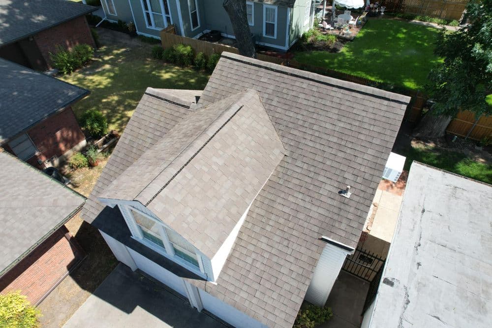 Aerial view of a residential roof with shingles and nearby homes in a suburban neighborhood.