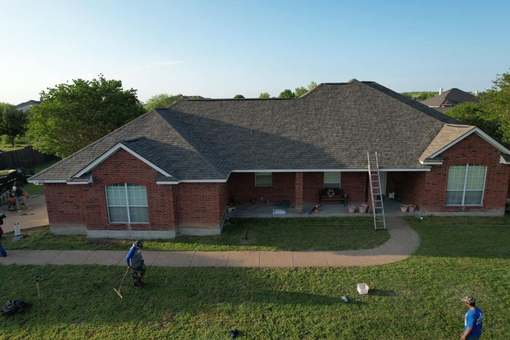 Aerial view of a red brick house with a newly installed roof and workers on the lawn.