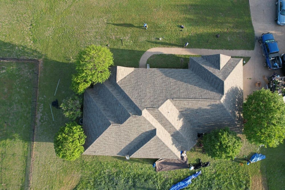 Aerial view of a house with a gray roof, surrounded by green grass and trees.