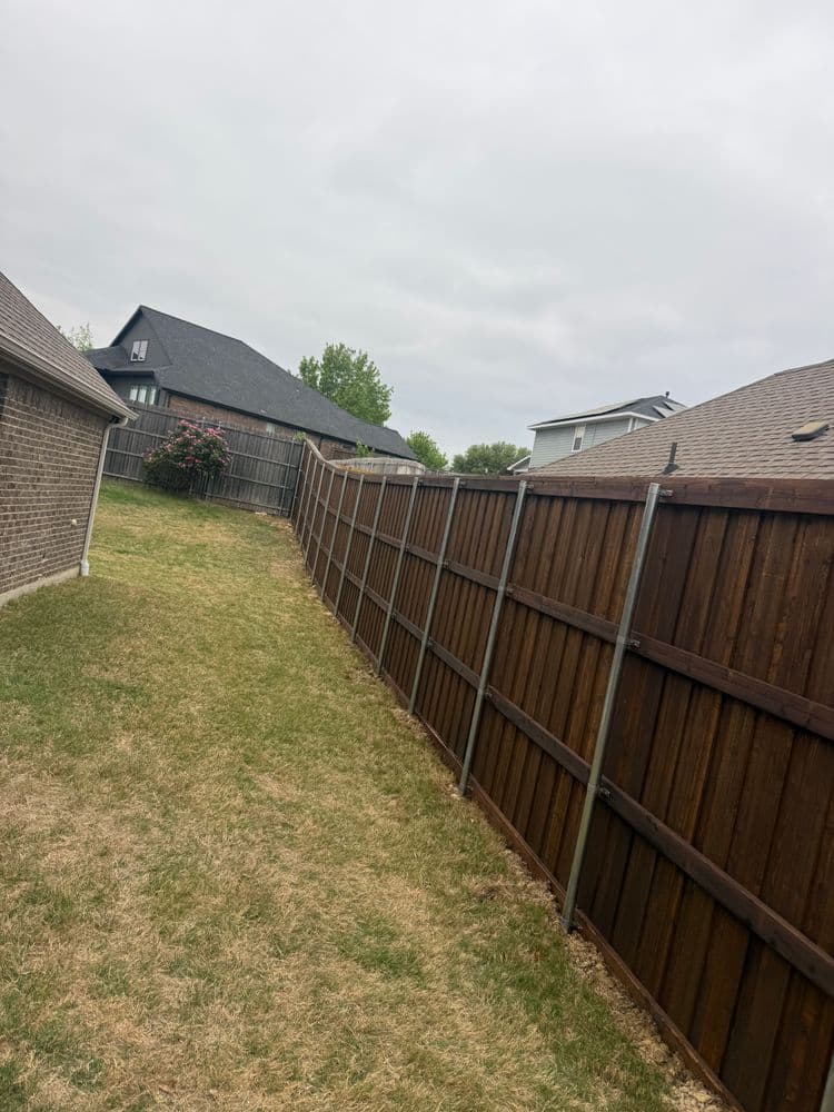 Residential backyard with wooden fence and lawn, cloudy sky in the background.