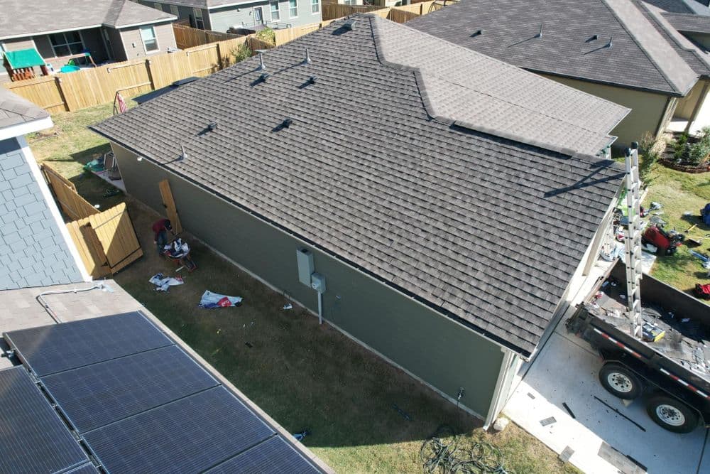 Aerial view of a home with new shingles and solar panels in a suburban neighborhood.