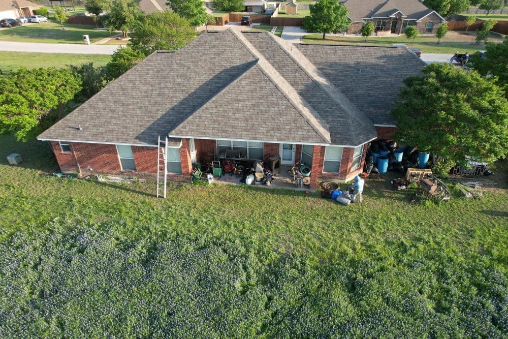 Aerial view of a house with a lawn, backyard clutter, and a ladder against the roof.