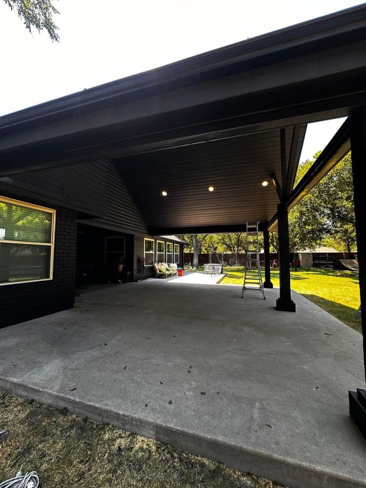 Covered patio with recessed lighting, ladder, and lush backyard view. Perfect outdoor space.