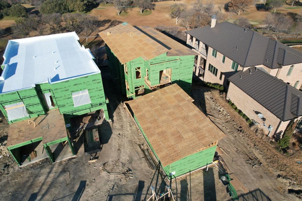 Aerial view of residential construction with two partially built homes and surrounding landscape.