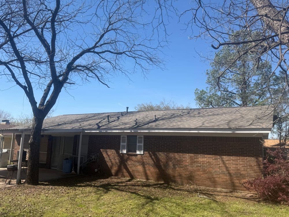 Brick house with a gray roof, surrounded by trees and clear blue sky.