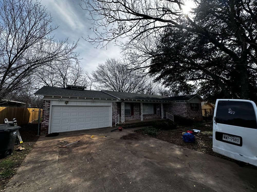 Single-story brick house with a garage, surrounded by bare trees and a cloudy sky.