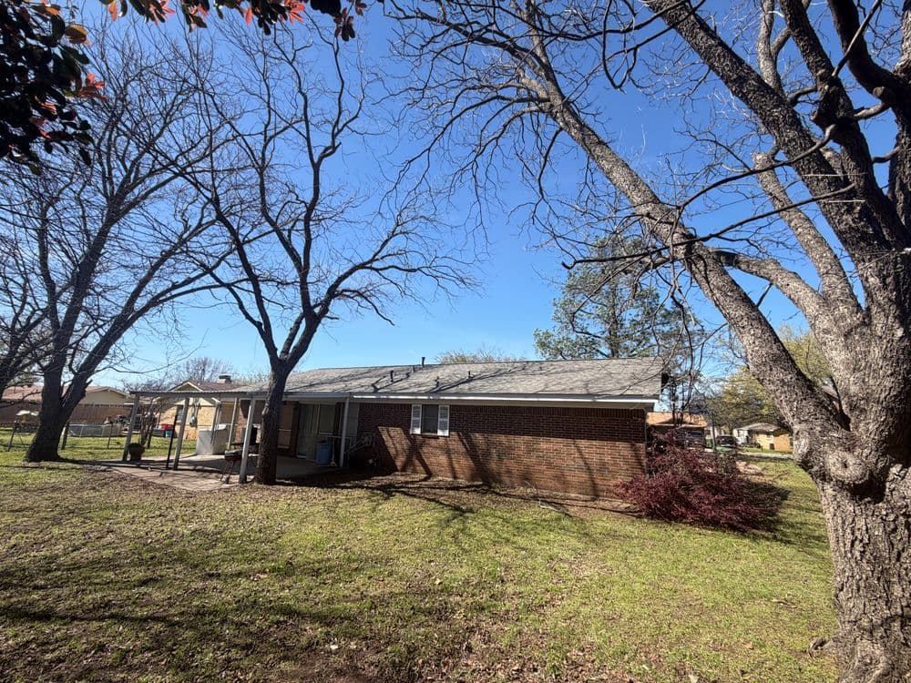 Single-story brick house with trees and clear blue sky in a residential area.