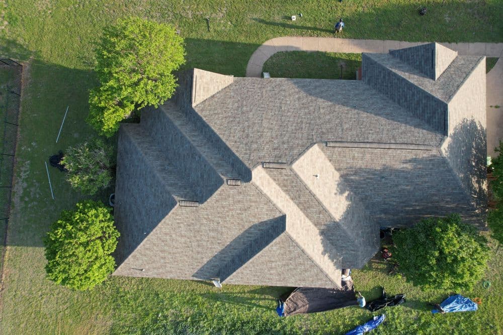 Aerial view of a residential roof with gray shingles and surrounding greenery.