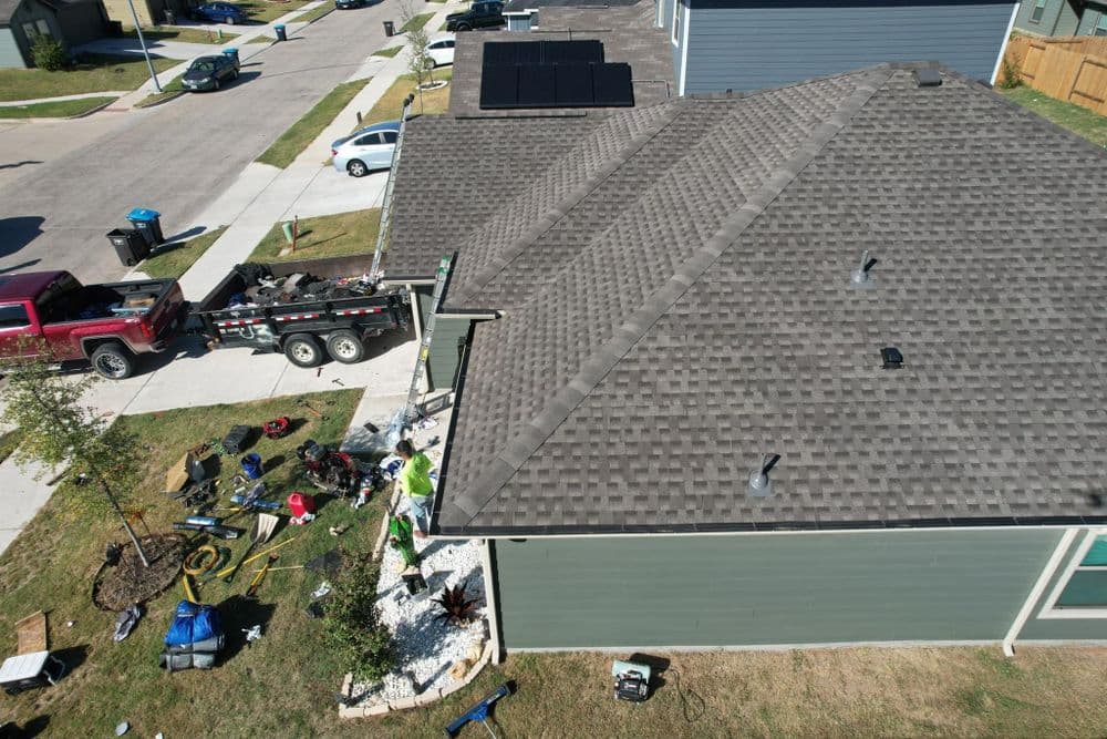 Aerial view of a house roof with solar panels, construction materials, and landscaping work nearby.