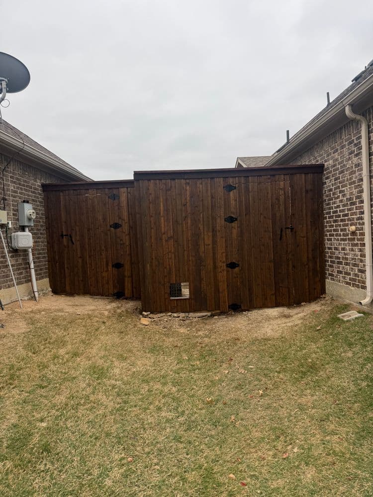 Wooden storage shed in backyard with a brick wall and grassy area.