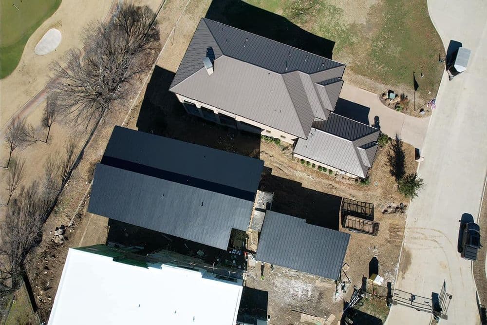 Aerial view of two large homes with rooftops, construction area, and golf course in background.