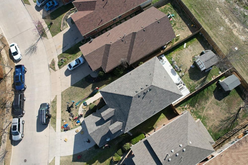 Aerial view of suburban homes with yards, cars parked, and outdoor activities visible.