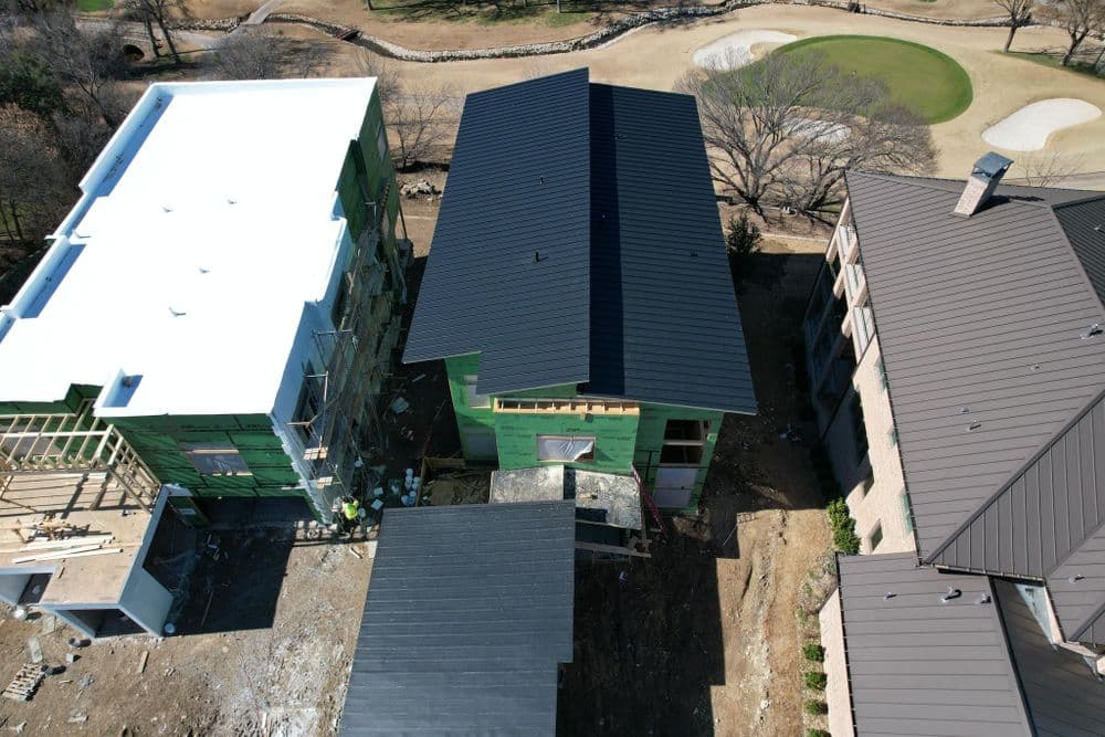 Aerial view of new construction homes with black metal roofs near a golf course.