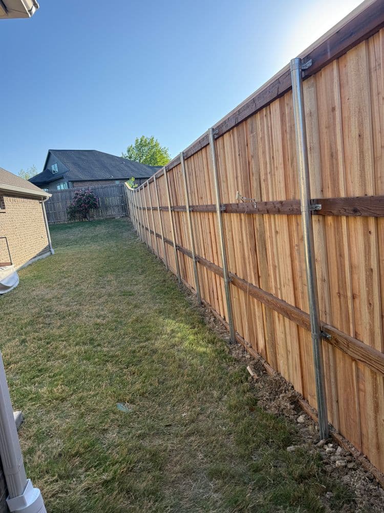 New wooden fence along a grassy yard, with blue sky and houses in the background.
