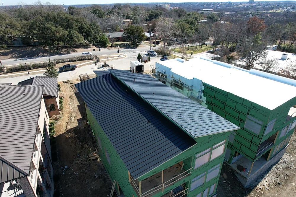 Aerial view of new construction featuring a black metal roof and green walls in a suburban area.