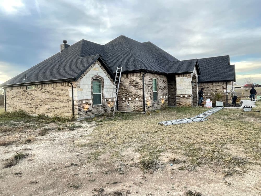 Home renovation project with a ladder, workers, and exterior brick and stone details.