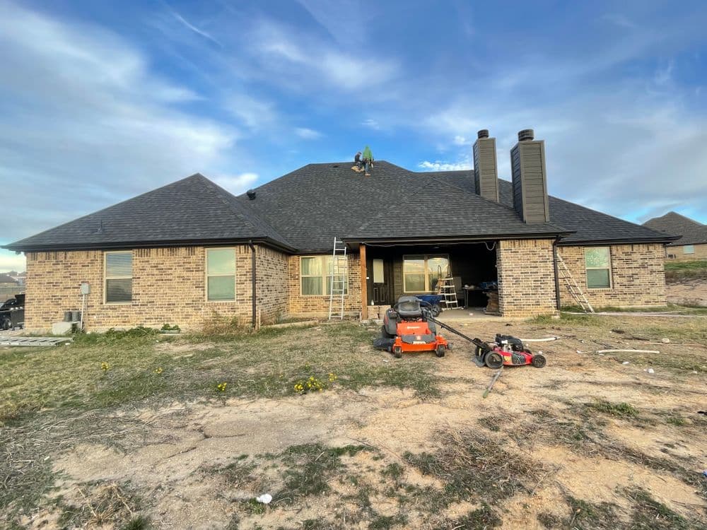 Roofing contractor working on a brick home with a black roof under a blue sky.