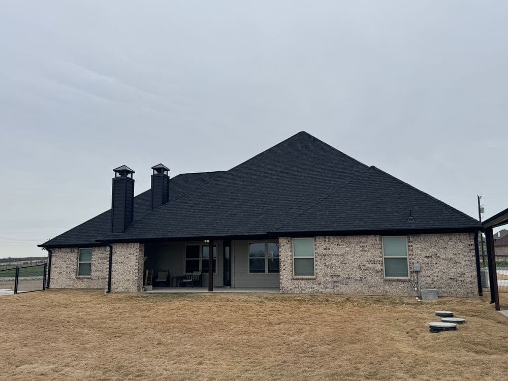 Modern single-story home with a black roof and brick exterior, set on a grassy lawn.
