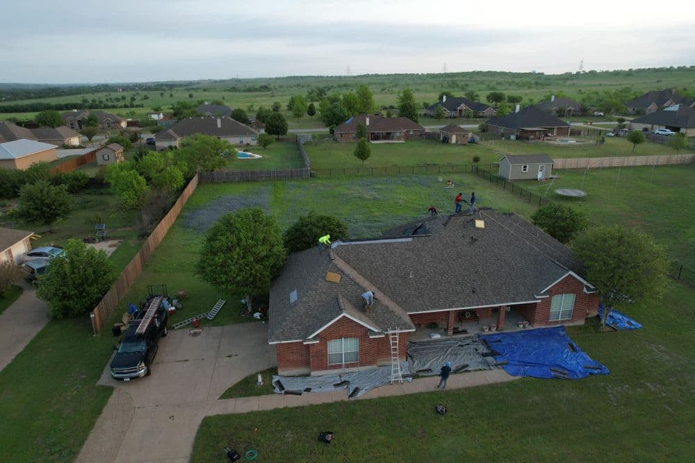 Aerial view of a residential roofing project in a suburban neighborhood with green lawns.