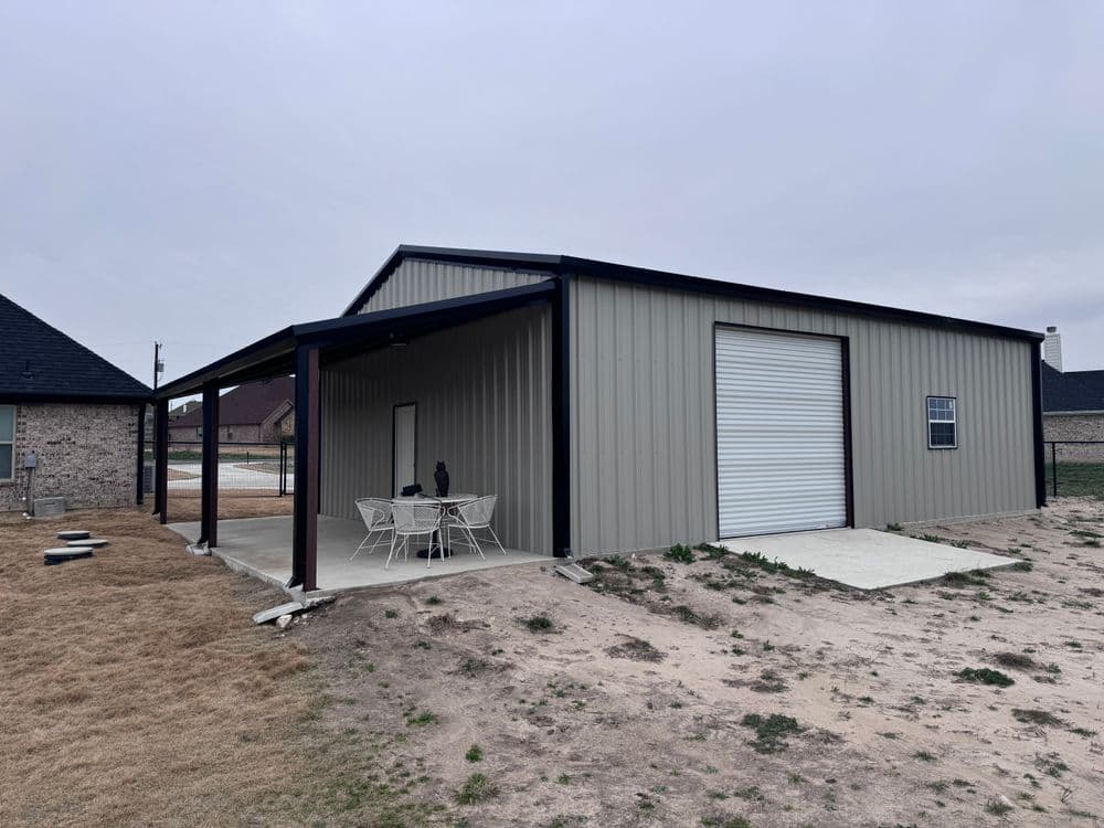 Metal shed with open porch, white chairs, and roll-up garage door in a residential area.