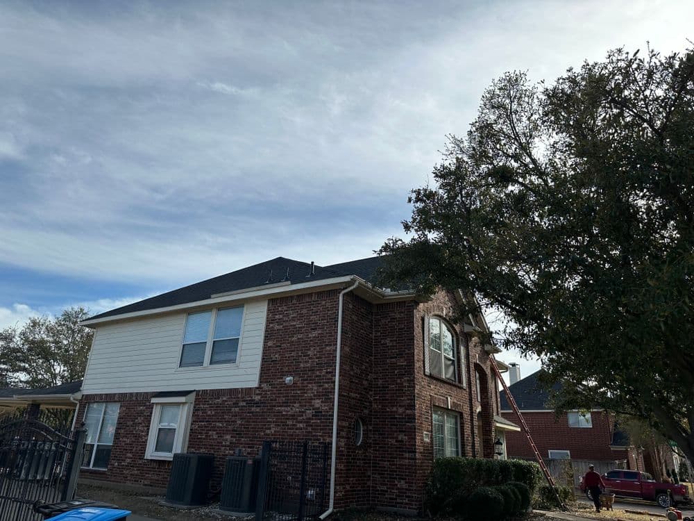 Two-story brick house with a white siding and trees under a cloudy sky.