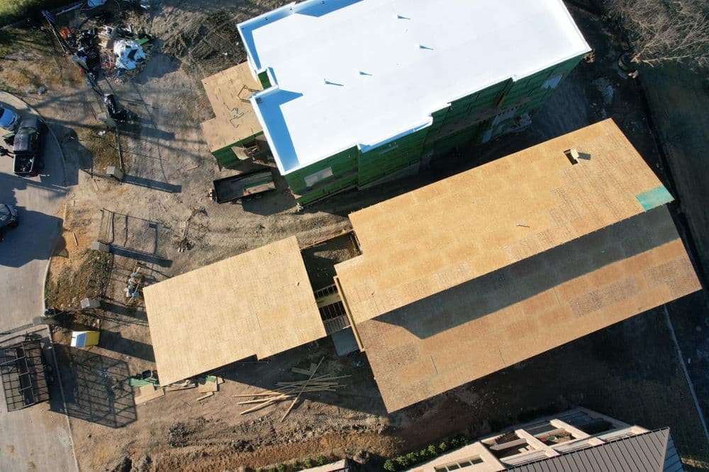 Aerial view of construction site with framed structures and materials on the ground.