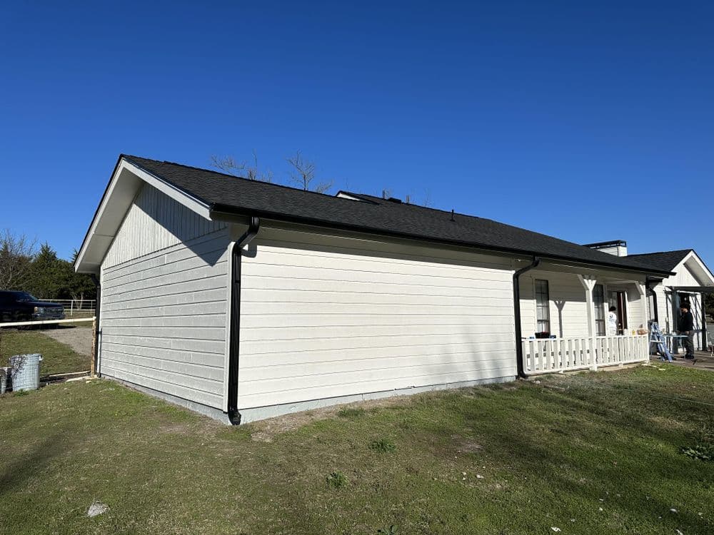 Side view of a modern house with new siding and a black roof against a clear blue sky.