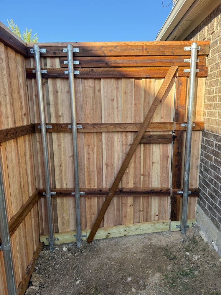 Wooden fence gate with metal supports and wooden accents in a backyard setting.