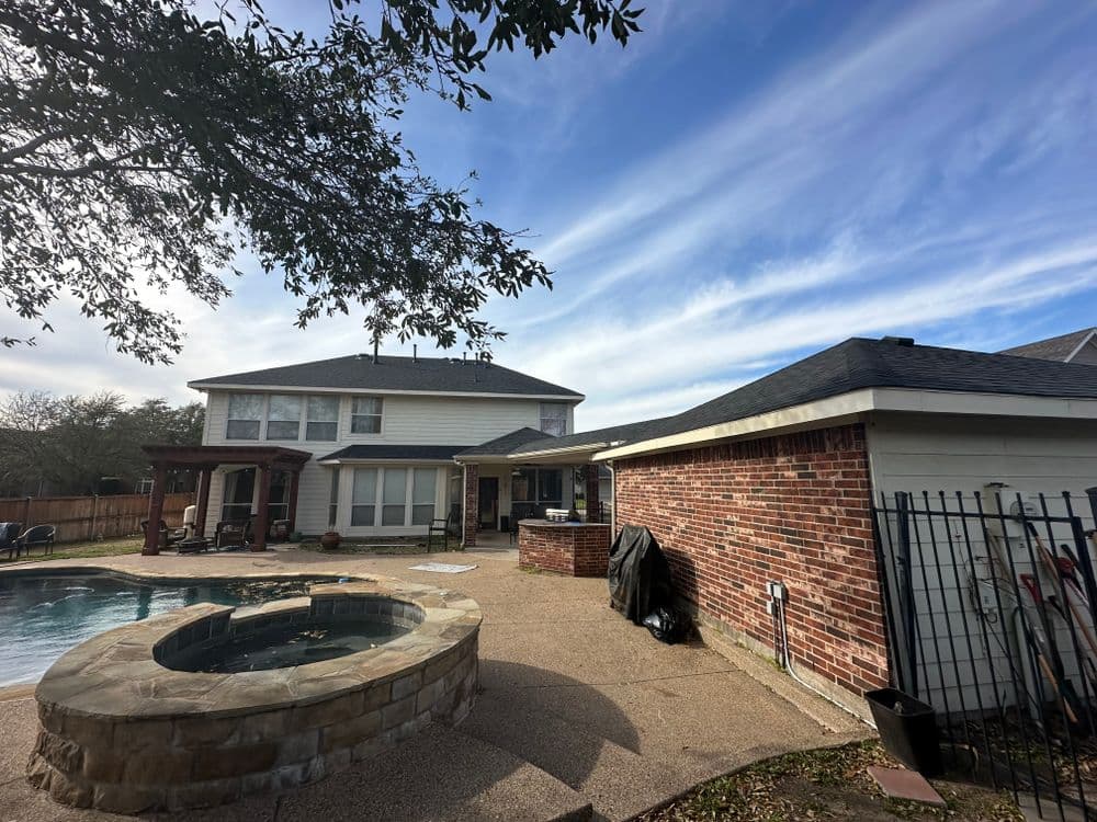 Backyard view with pool, spa, and two-story house under a blue sky with scattered clouds.