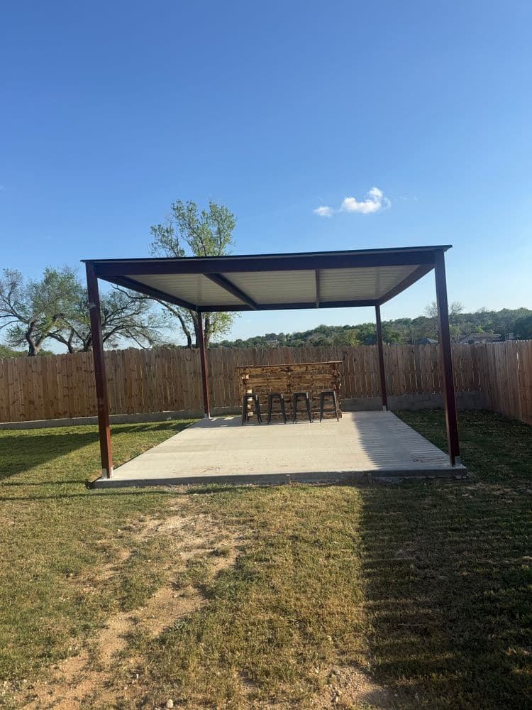 Backyard patio with metal roof and wooden bar seating under blue sky and wooden fence.