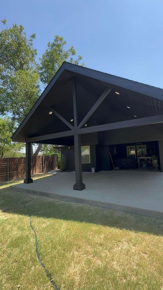 Modern patio design with a large overhang and ceiling lights, surrounded by greenery.