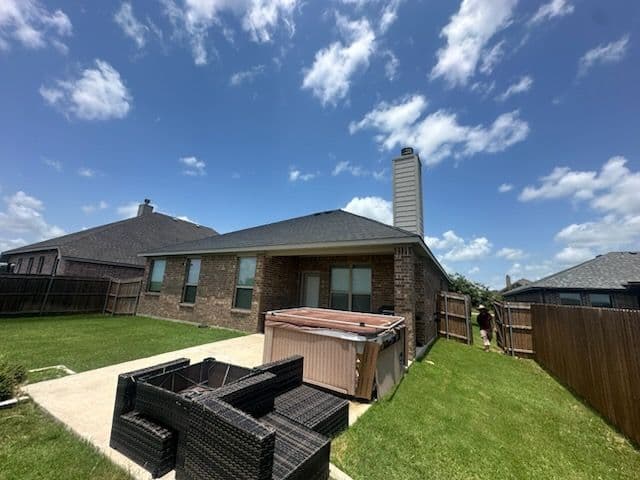 Backyard with a hot tub, patio furniture, and clear blue sky in a residential area.