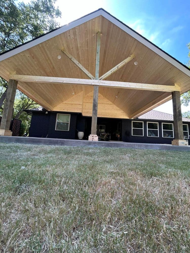 Modern home exterior with wooden overhang and support beams, featuring a landscaped yard.