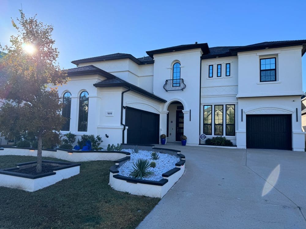 Modern white luxury home with black accents and landscaped front yard. Sunny day, clear sky.