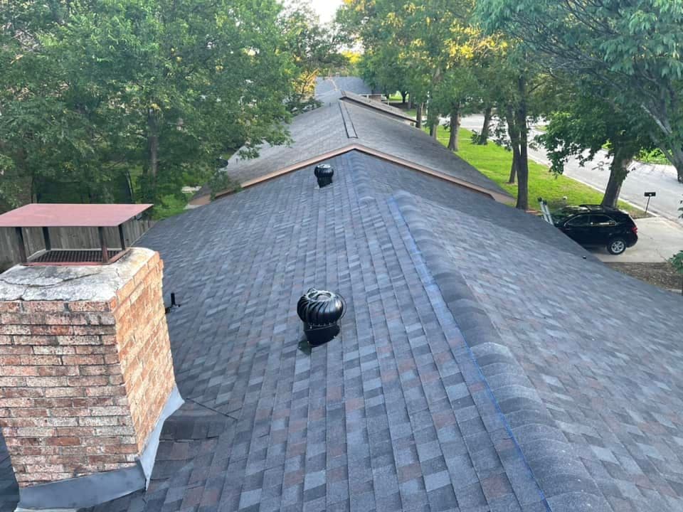 Aerial view of a residential roof with shingles, chimney, and ventilation systems.