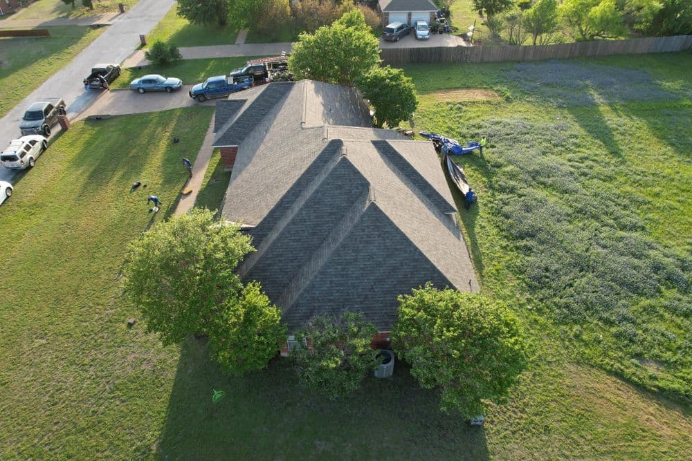 Aerial view of a residential home with a sloped roof and surrounding green landscape.