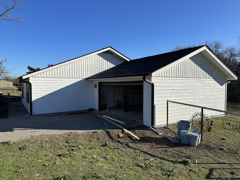 White house exterior with garage and clear blue sky, surrounded by grassy yard.