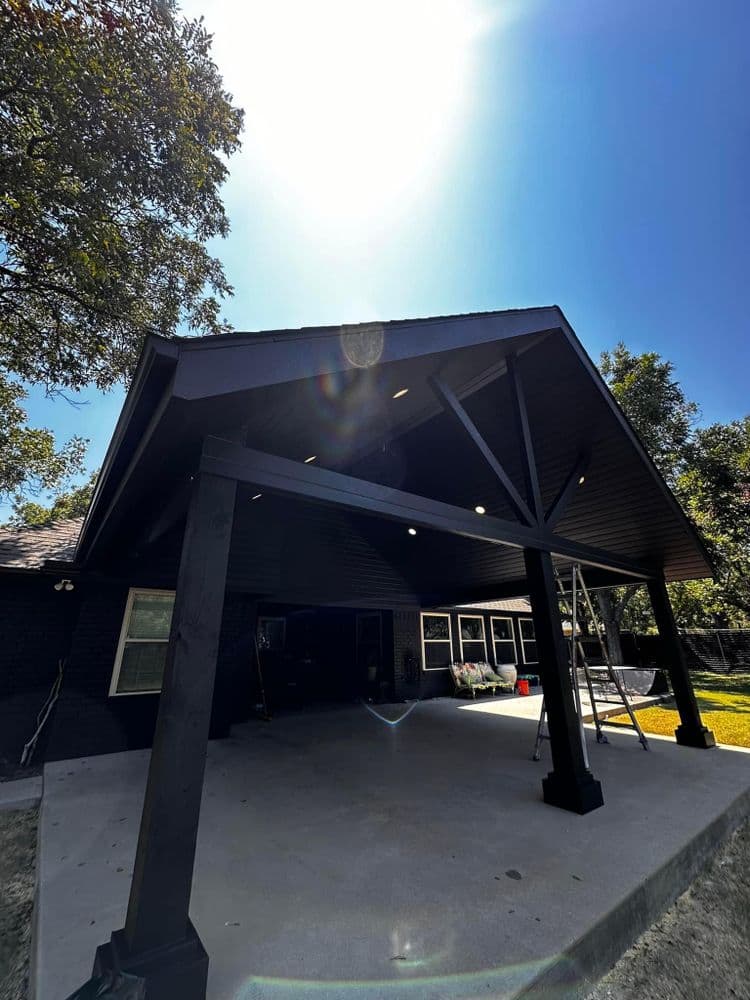 Modern black patio with wooden beams under bright sunlight, ideal for outdoor gatherings.