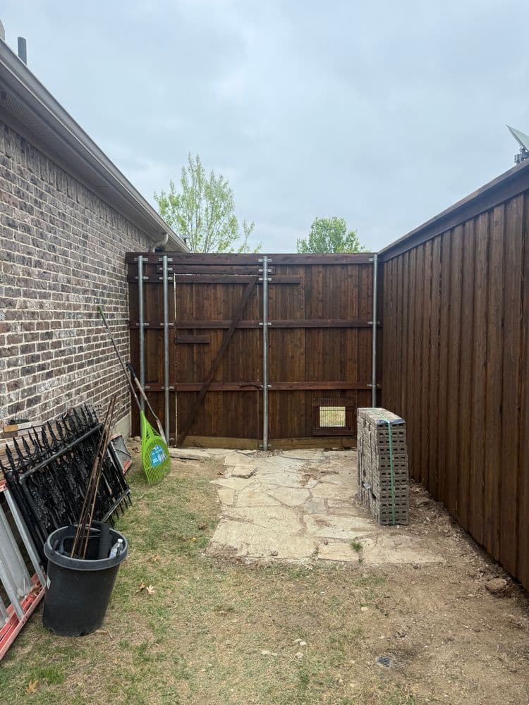 Wooden fence construction with stone pathway and tools in a backyard setting.