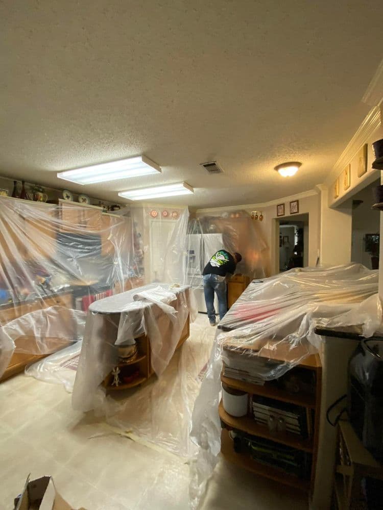 Kitchen renovation in progress with plastic covering appliances and furniture for protection.