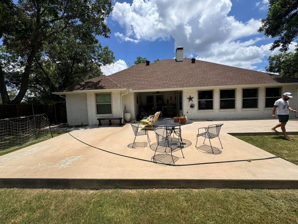 Outdoor patio with dining set, grassy area, and a residential home under a blue sky.