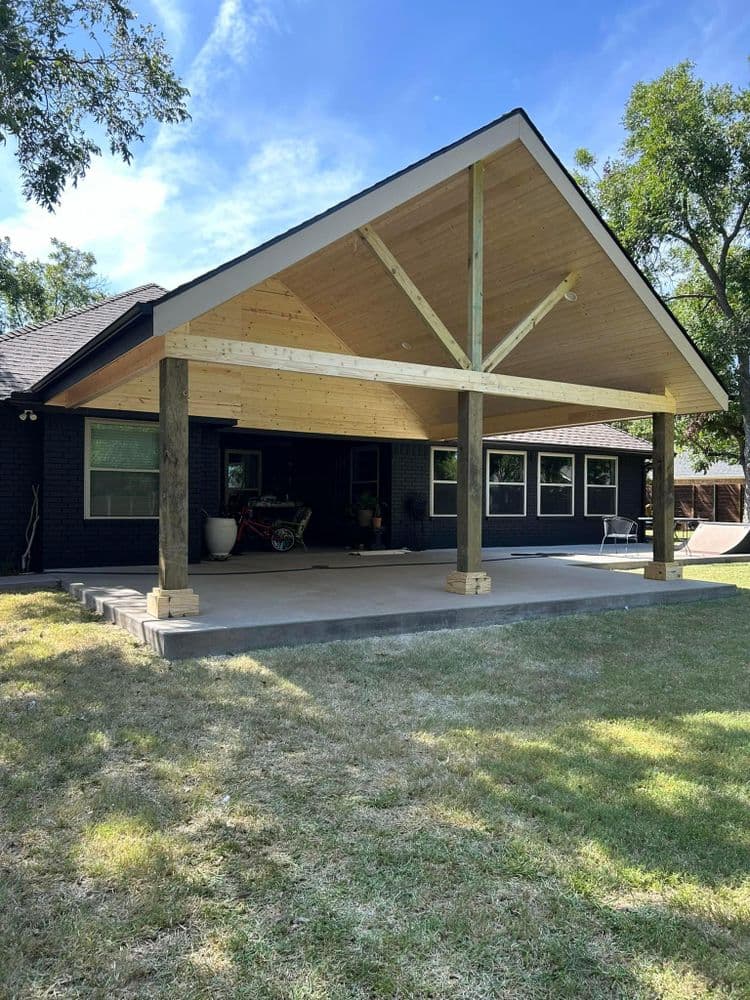 Modern outdoor patio with a pitched roof, wooden beams, and spacious lawn.